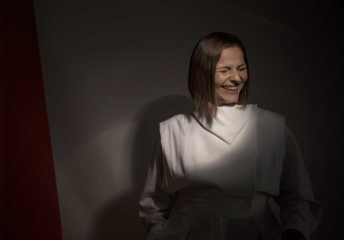 Frau in weißer Bluse im weichen Lichtkegel vor dunkler Wand