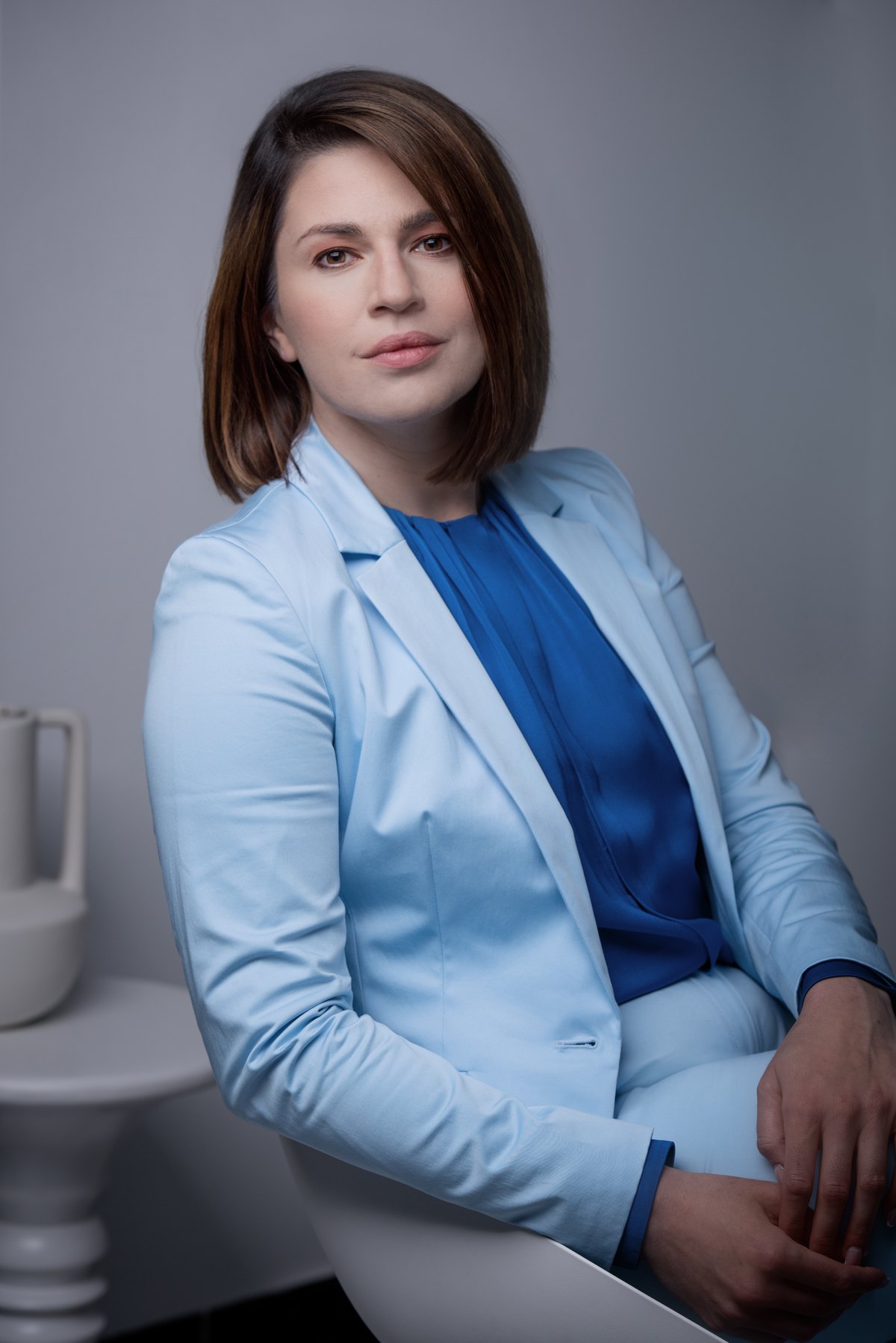 Frau im hellblauen Blazer sitzt vor hellblauem Hintergrund