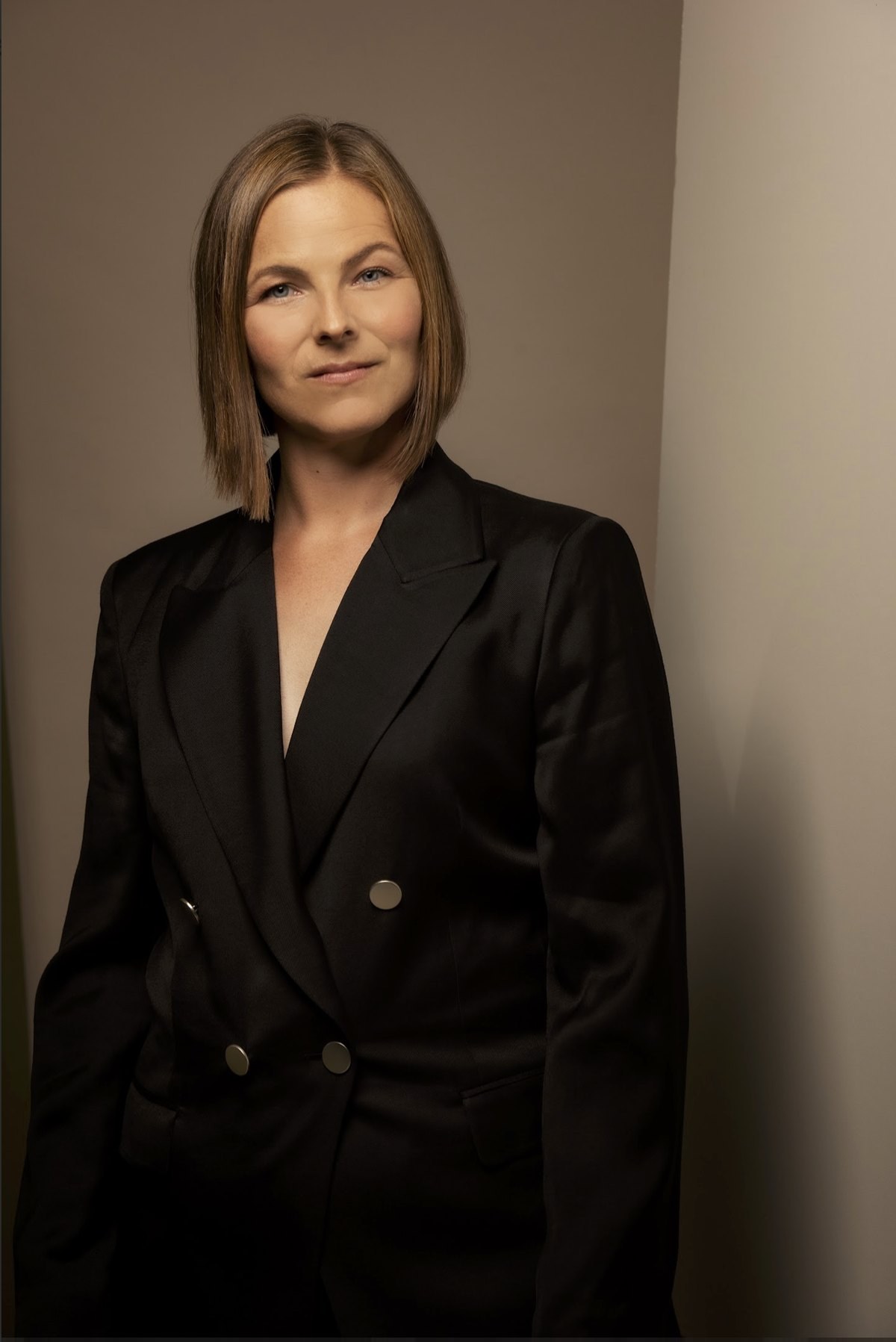 Portrait einer Frau im schwarzen Blazer vor warm beleuchteter Wand