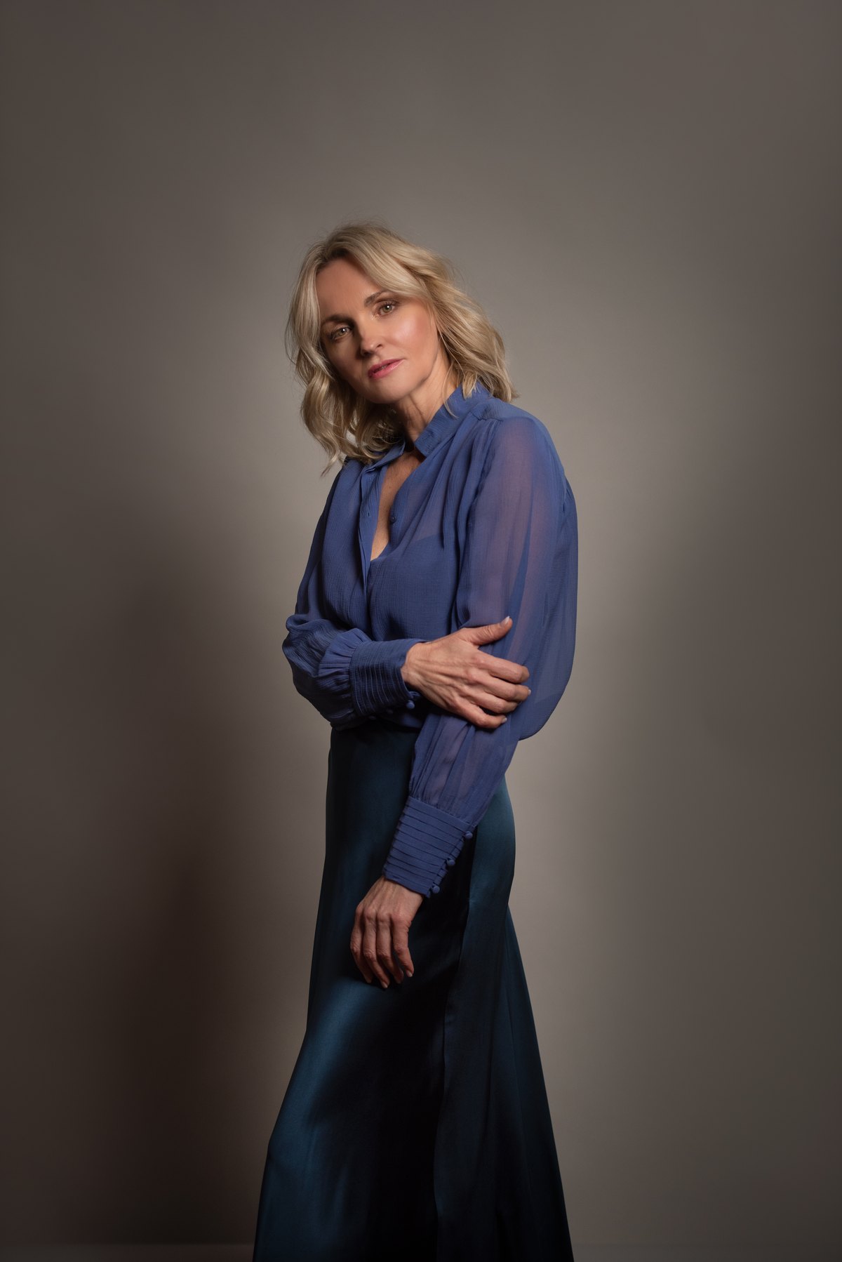 Frau in blauer Bluse steht vor warmgrauem Studiohintergrund