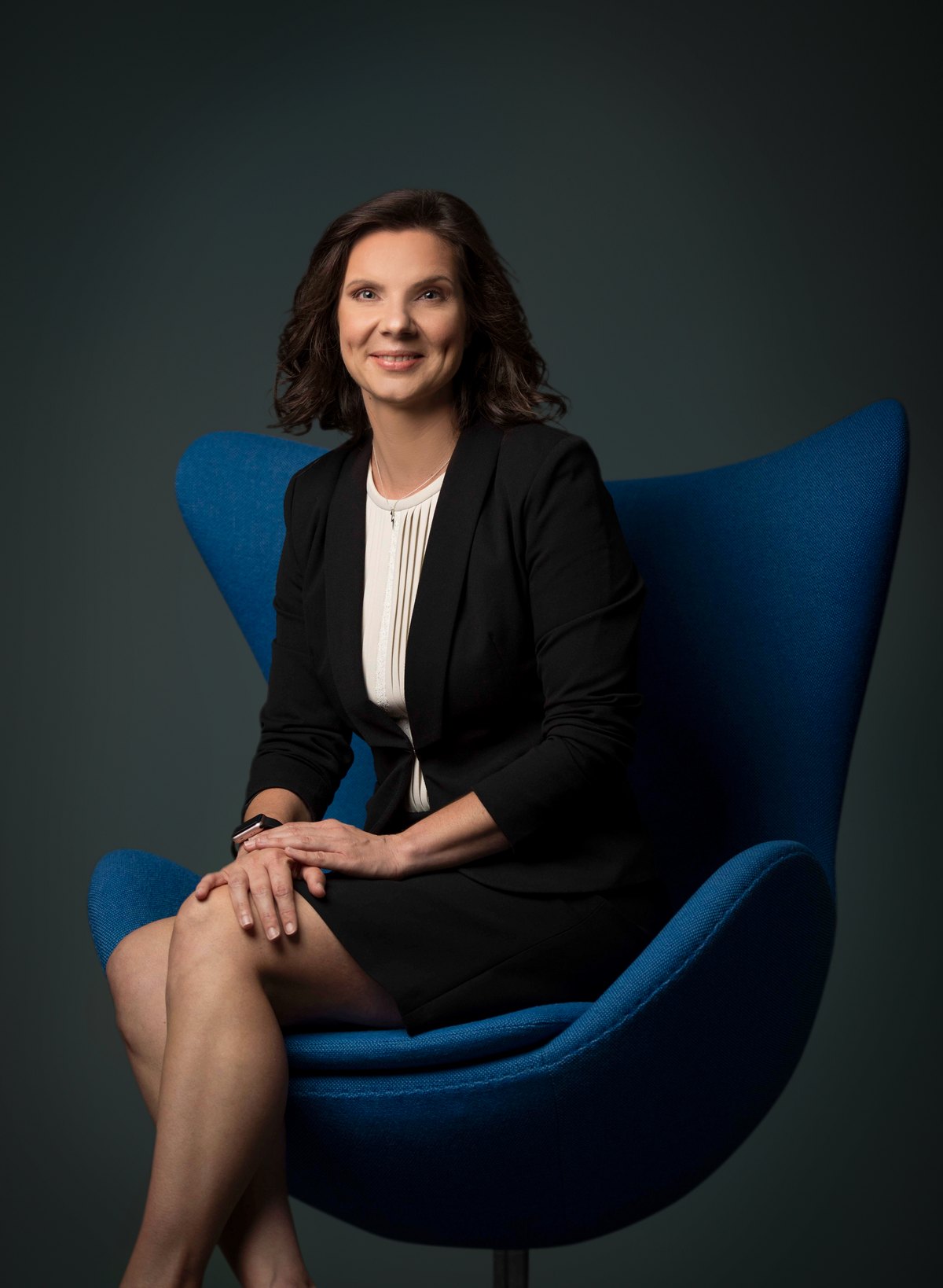 Frau im schwarzen Kostüm sitzt in einem blauen Designsessel