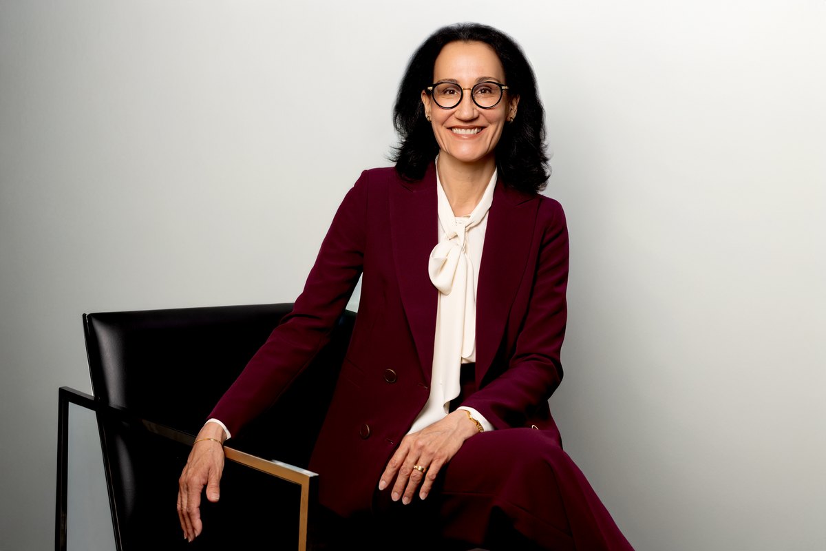 Frau im bordeauxroten Anzug mit Brille auf einem Designstuhl