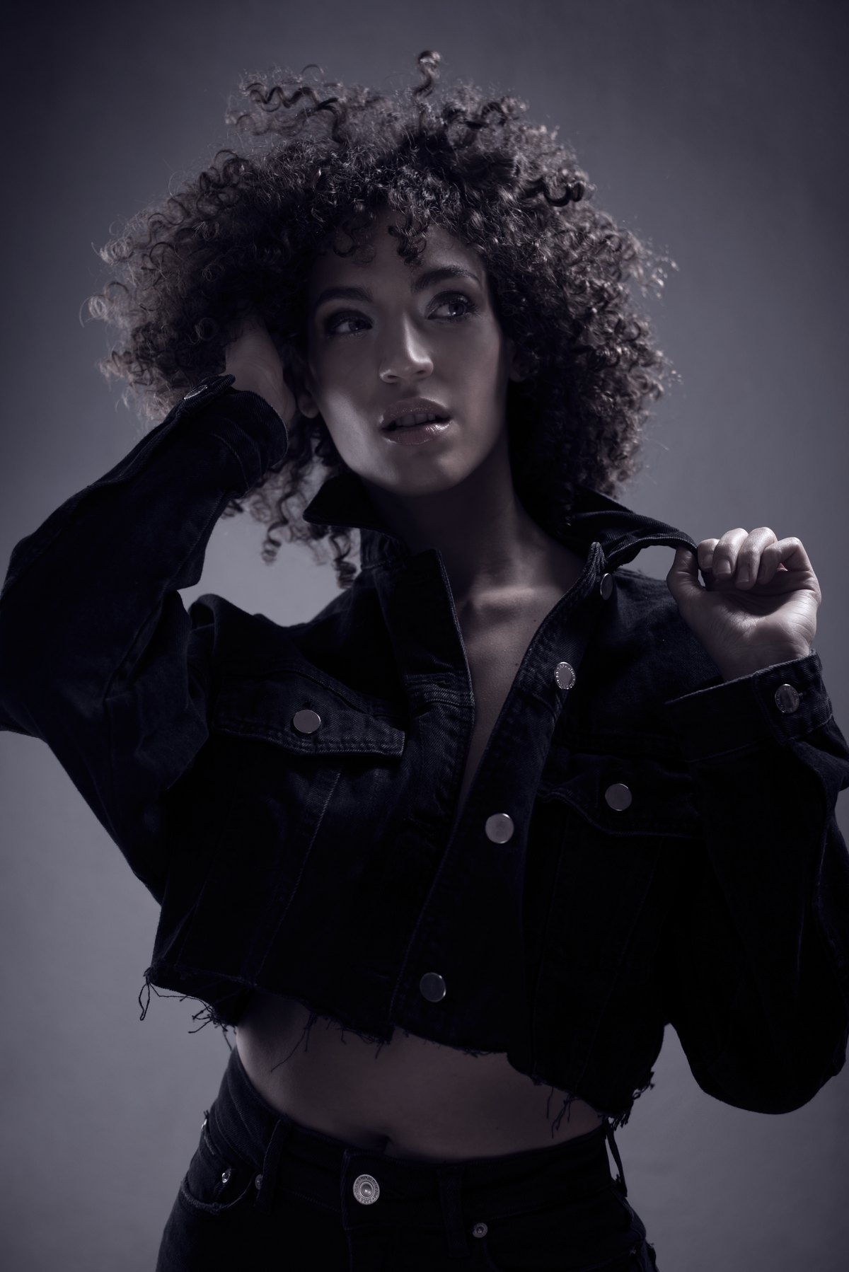 Frau in Jeansjacke mit Locken vor dunklem Hintergrund
