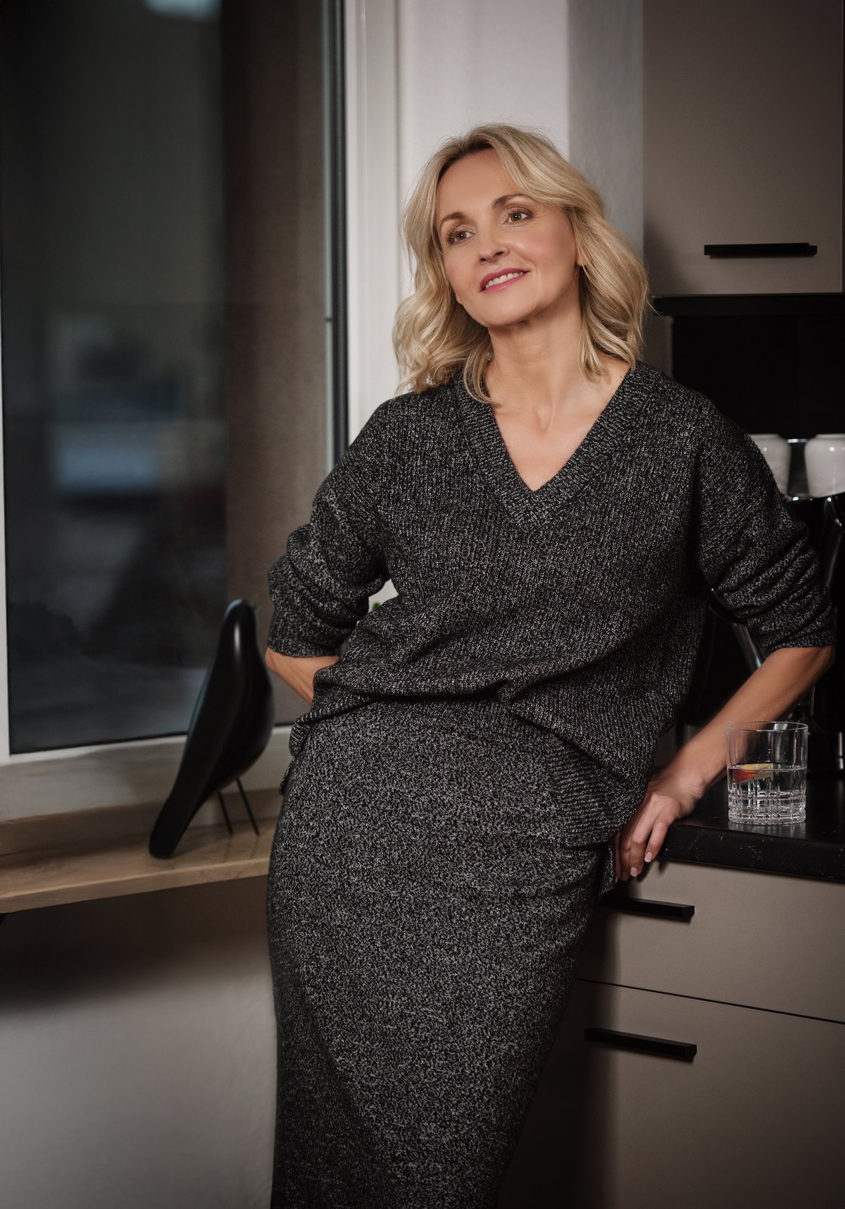 Frau im grauen Strickkleid steht in einer hellen Küche