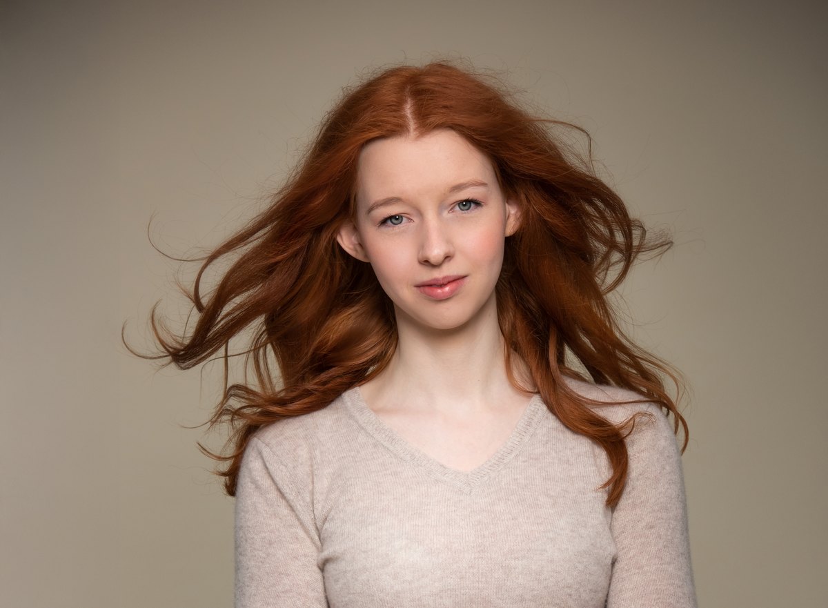 Portrait einer jungen Frau mit langen roten Haaren vor Beige