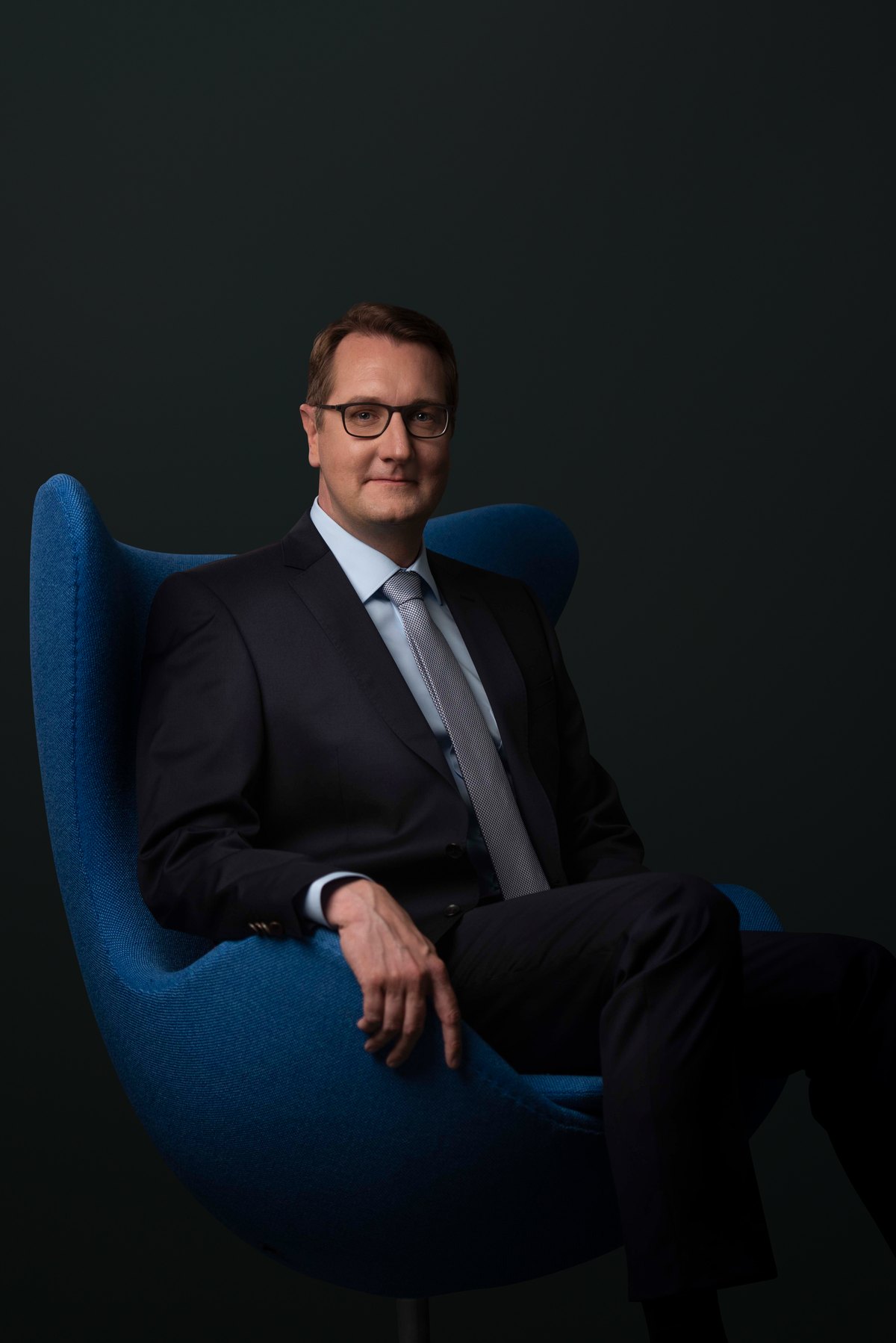 Mann im Anzug sitzt in einem blauen Designsessel