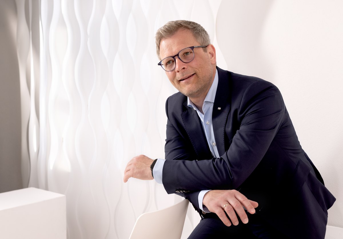 Mann mit Brille im Anzug sitzt vor gewellter weißer Wand