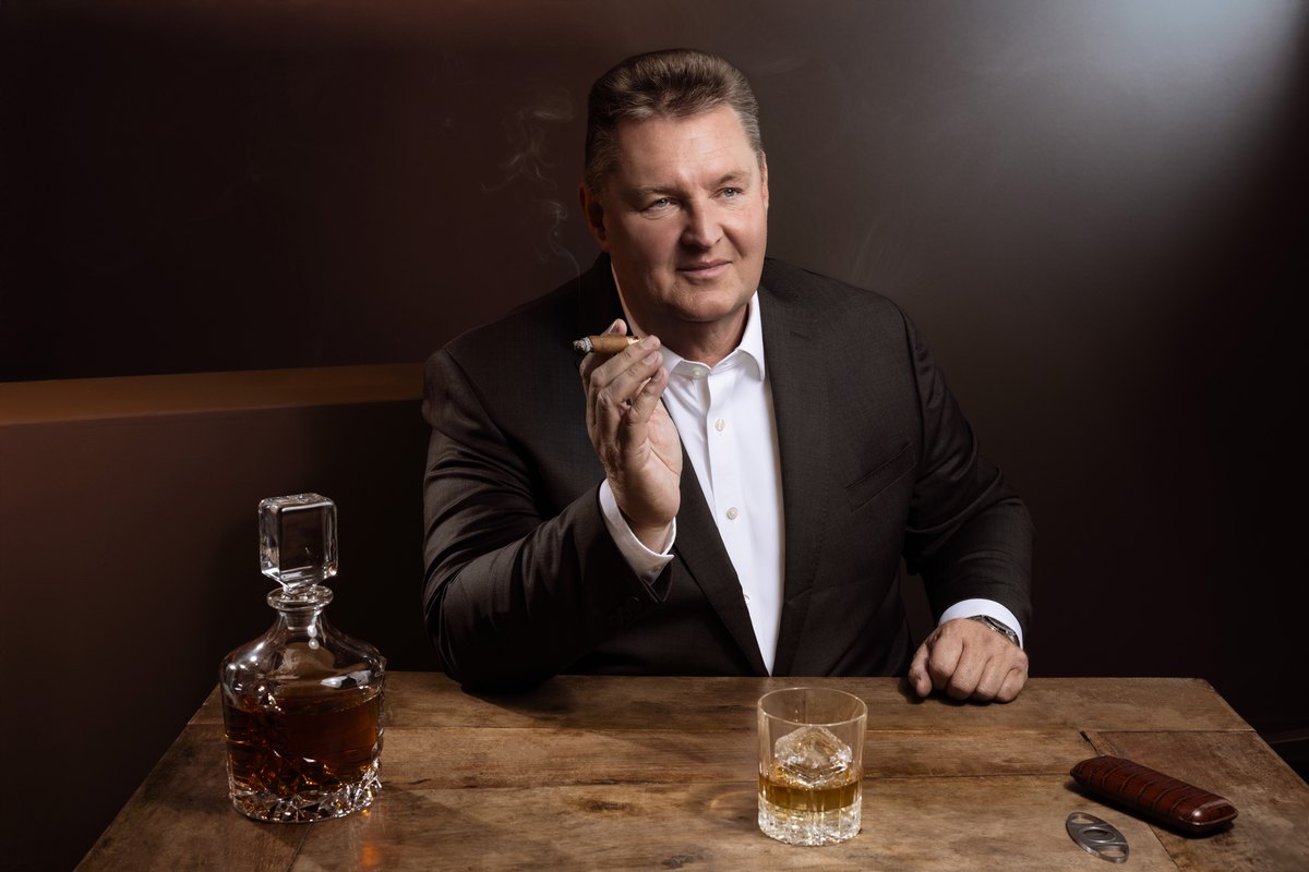Mann im Sakko am Tisch mit Karaffe und Glas in warmem Licht