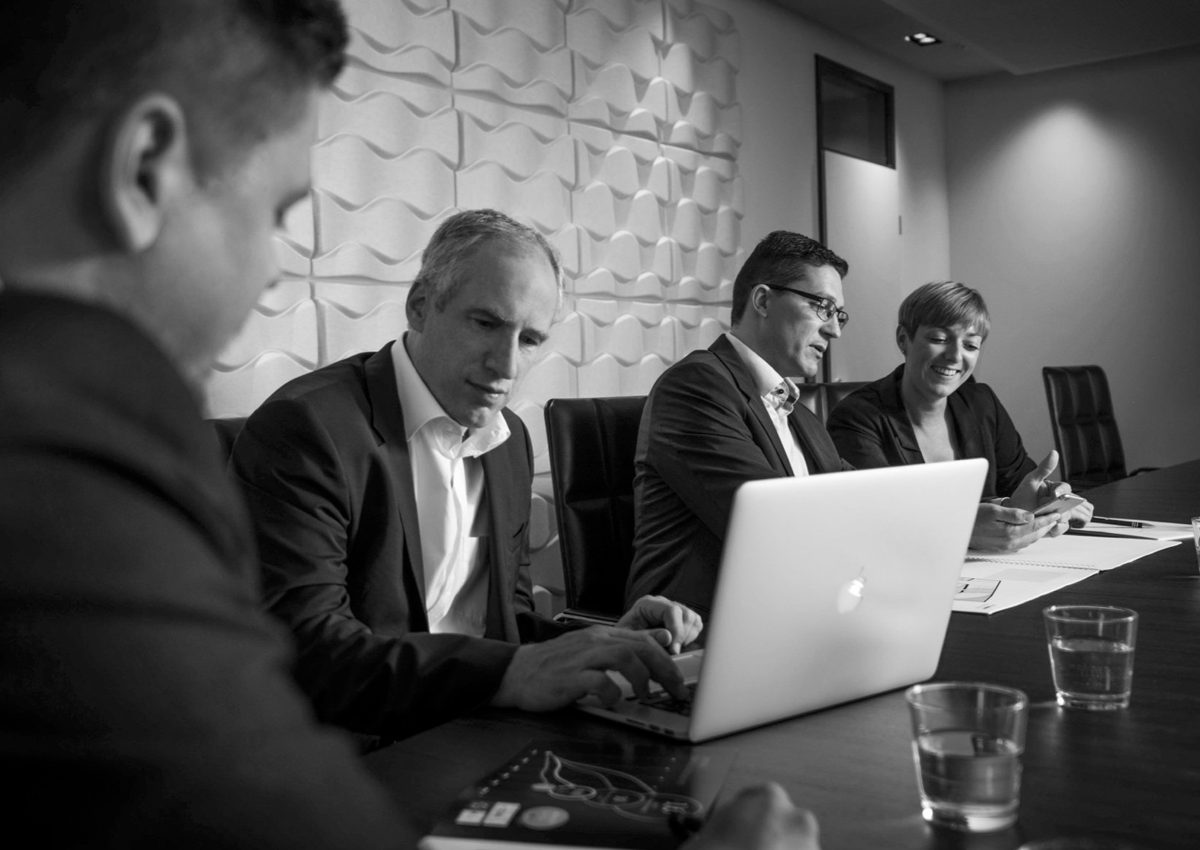 Schwarzweisse Aufnahme einer Besprechung mit vier Personen am Konferenztisch mit Laptop