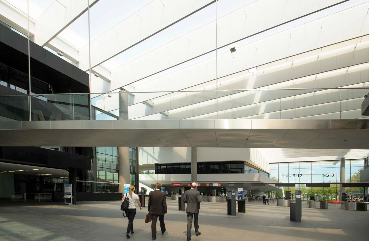 Drei Personen in Businesskleidung gehen durch eine helle Messehalle mit Lichtdecke