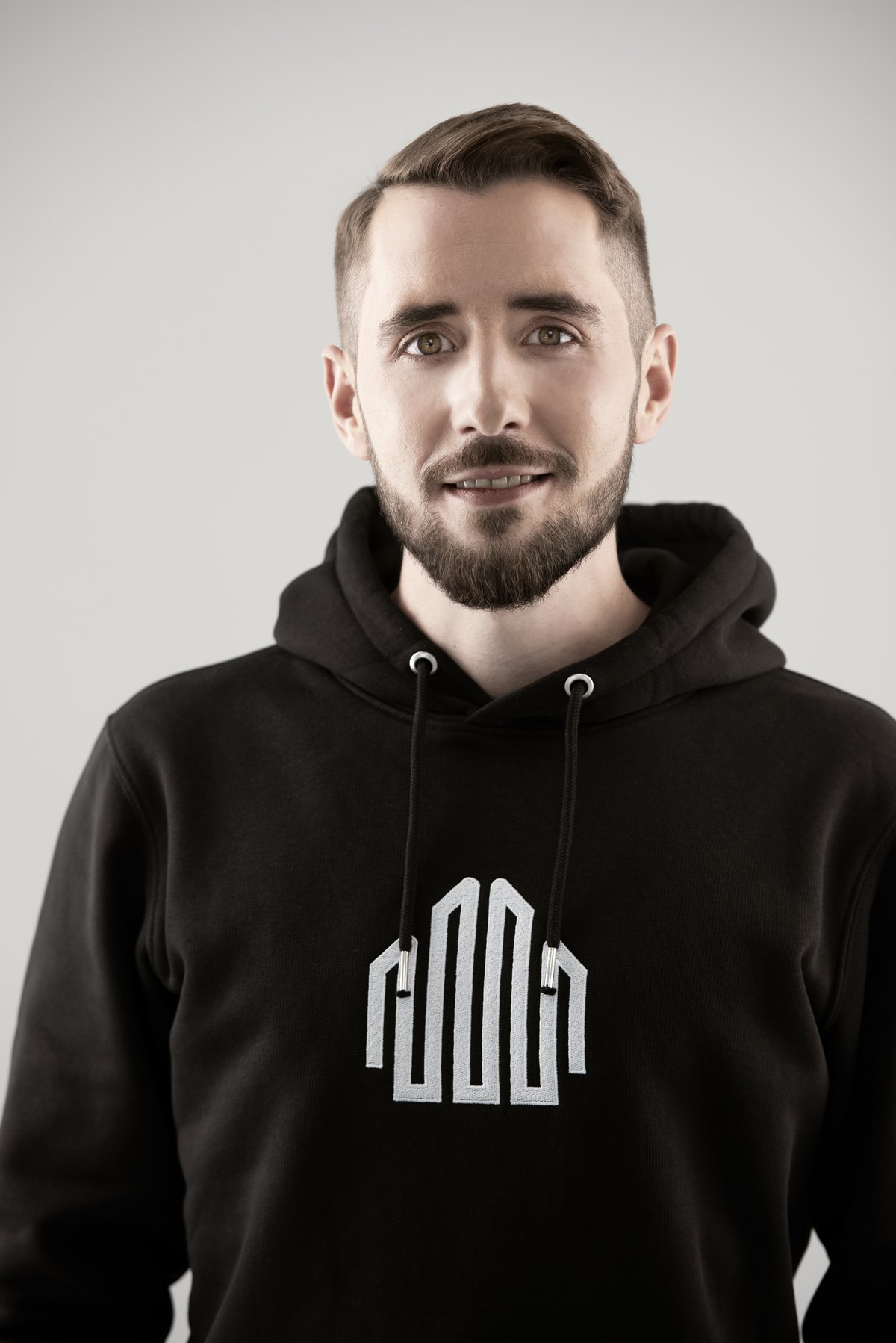 Portrait eines Mitarbeiters im schwarzen Hoodie mit Firmenlogo