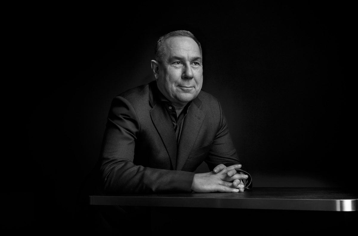 Schwarzweisses Low-Key-Businessportrait eines Mannes im Sakko an einem Tisch