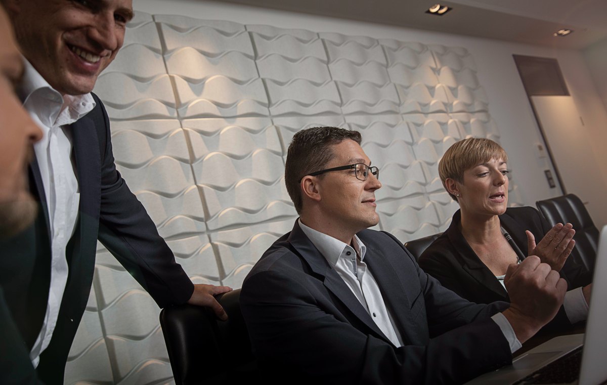 Lachendes Team am Konferenztisch vor weißer Strukturwand