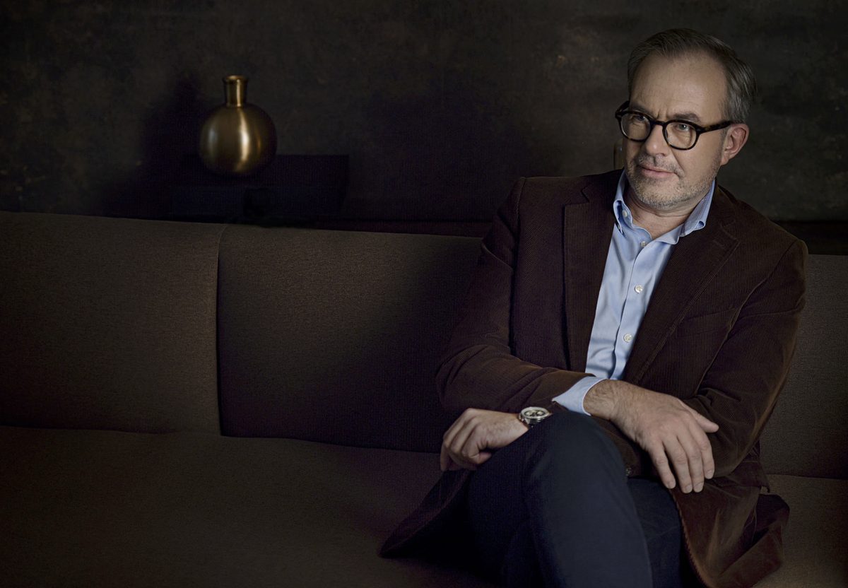 Mann mit Hornbrille und braunem Cordsakko sitzt auf einem Sofa