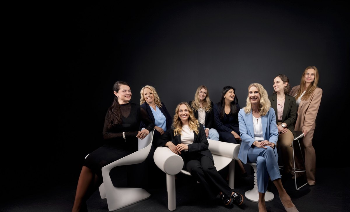 Acht Frauen in Businesskleidung gruppiert auf weißem Möbel vor schwarzem Hintergrund