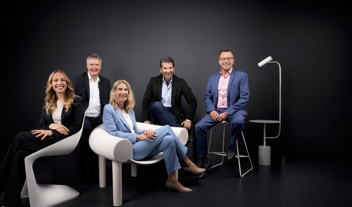 Fünfköpfiges Team in Business-Kleidung gruppiert um weiße Designmöbel vor dunklem Hintergrund