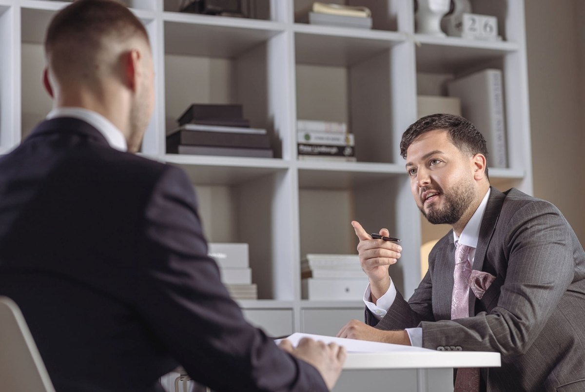 Zwei Männer im Anzug im Gespräch an einem Schreibtisch im Büro