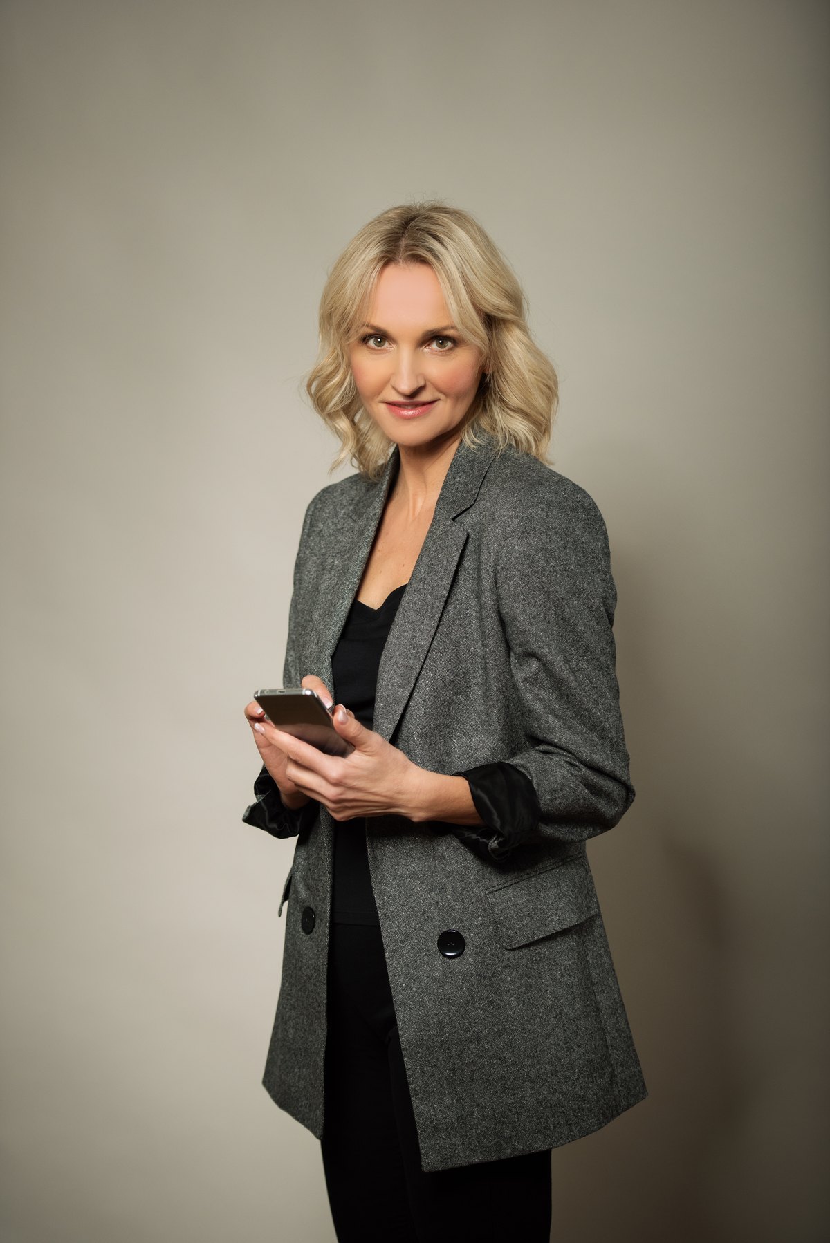Frau im grauen Blazer mit Smartphone vor beigem Hintergrund