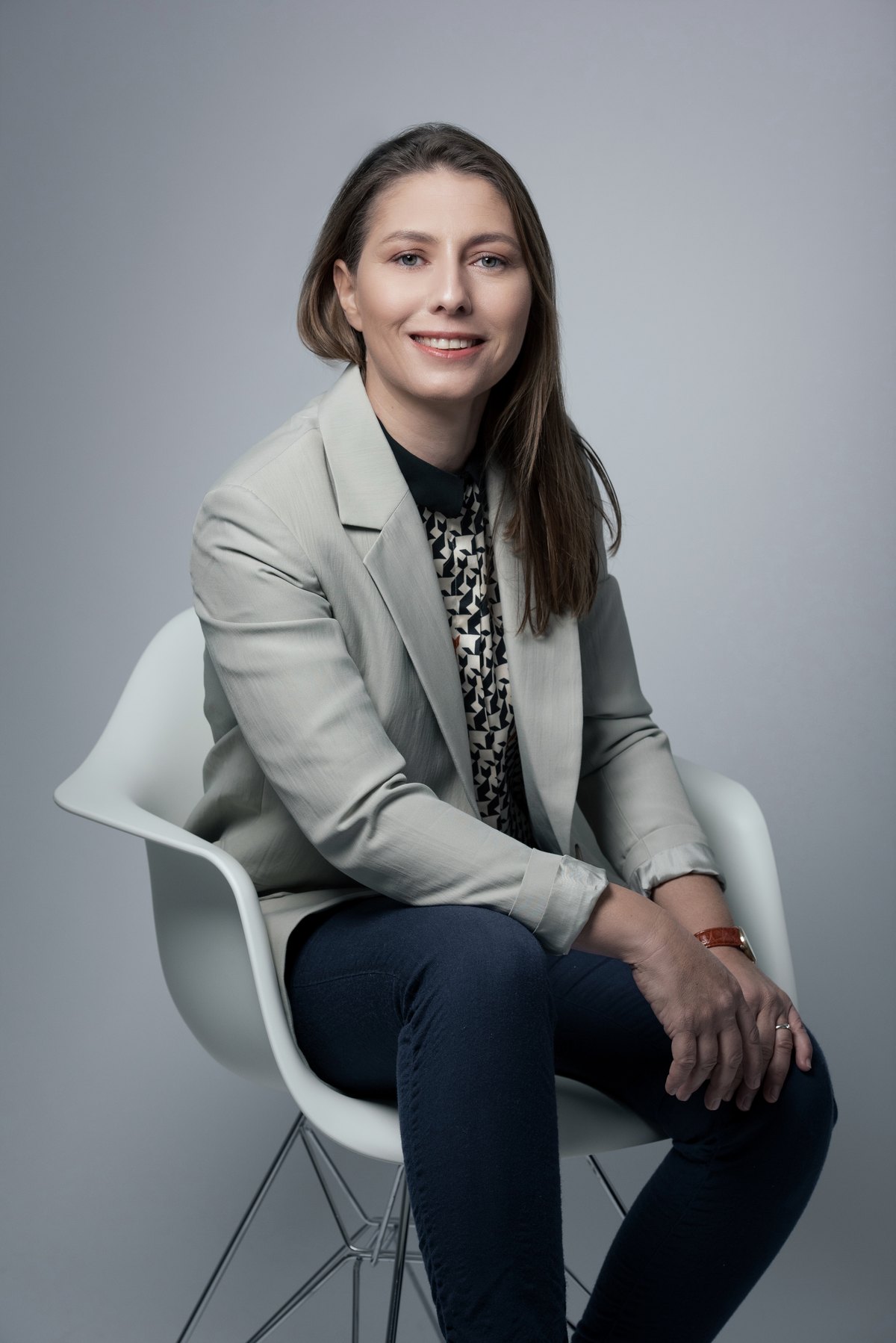 Frau im hellen Blazer sitzt auf einem weißen Schalenstuhl