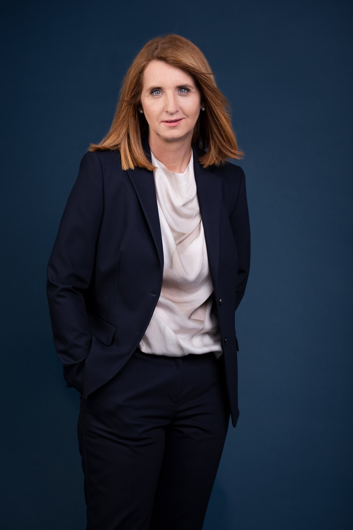 Frau im dunklen Hosenanzug vor blauem Hintergrund