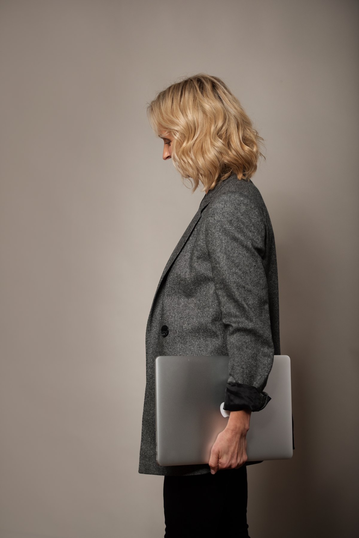 Frau im grauen Blazer im Profil mit Laptop unter dem Arm
