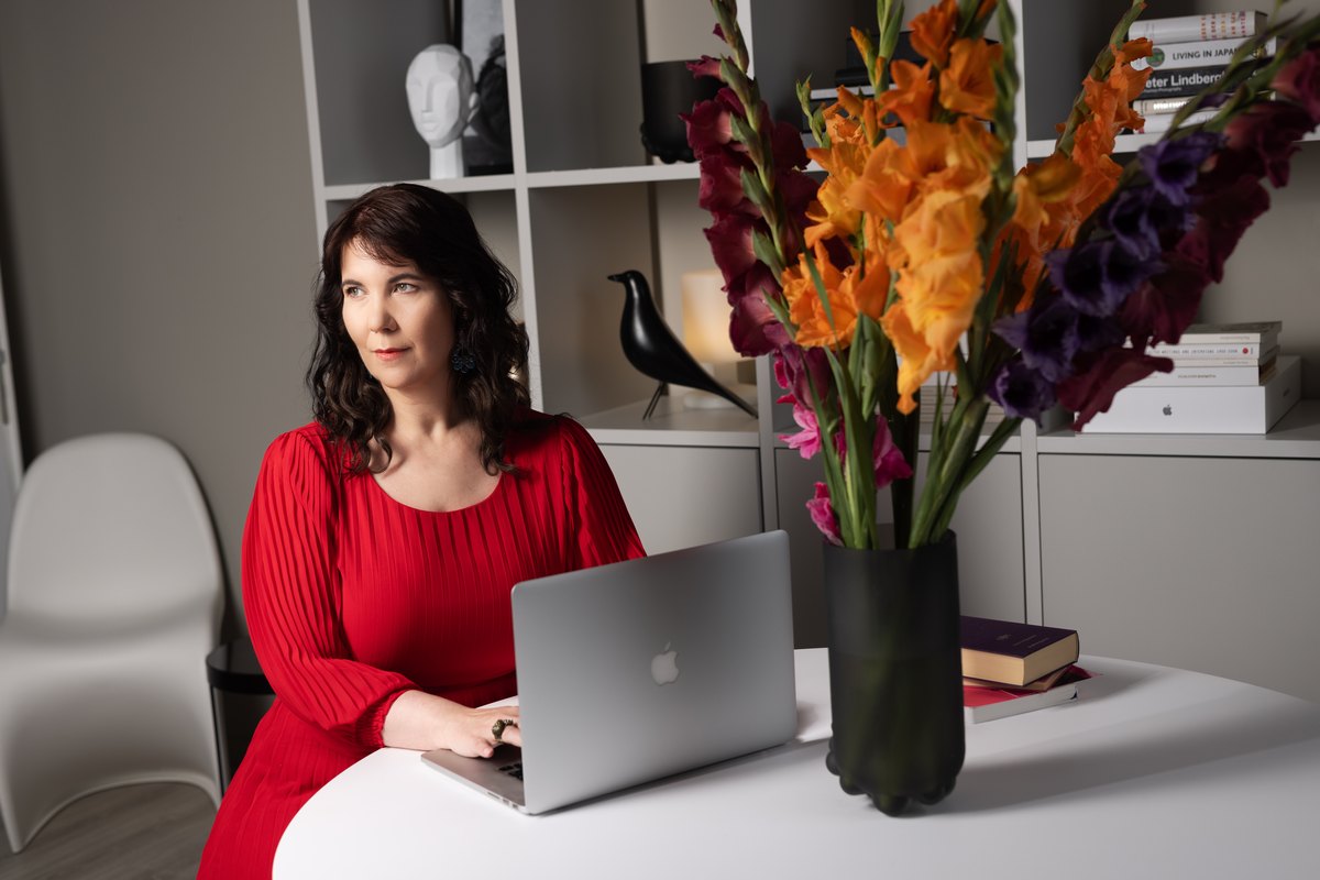Frau in rotem Oberteil am Laptop neben einem Gladiolenstrauss