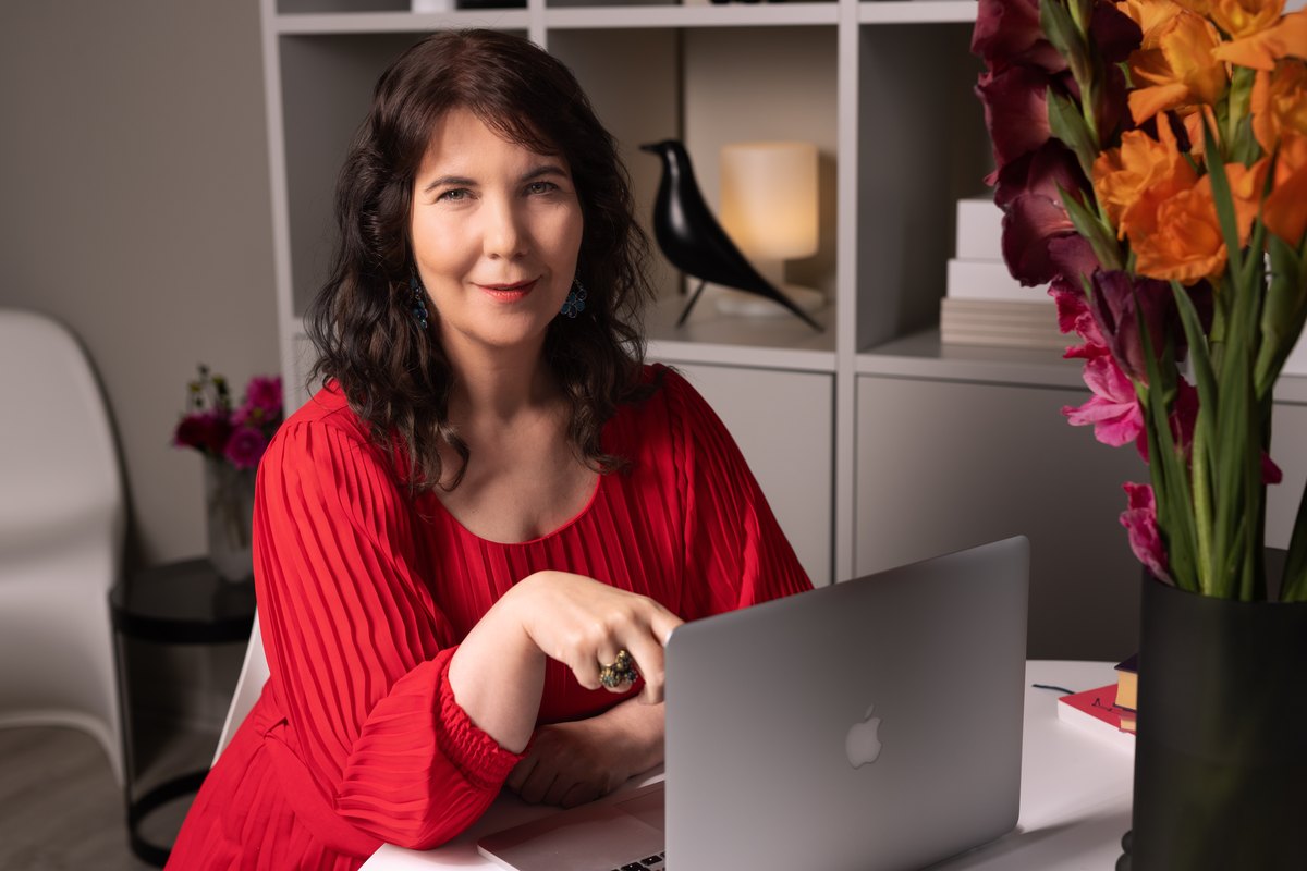 Frau in rotem Oberteil arbeitet am Laptop, Blumen im Vordergrund