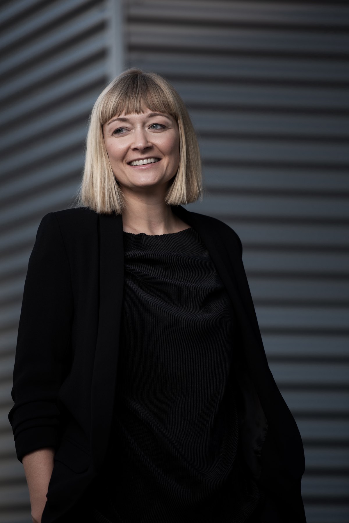 Ganzkörperportrait einer Frau in Schwarz vor Metallfassade