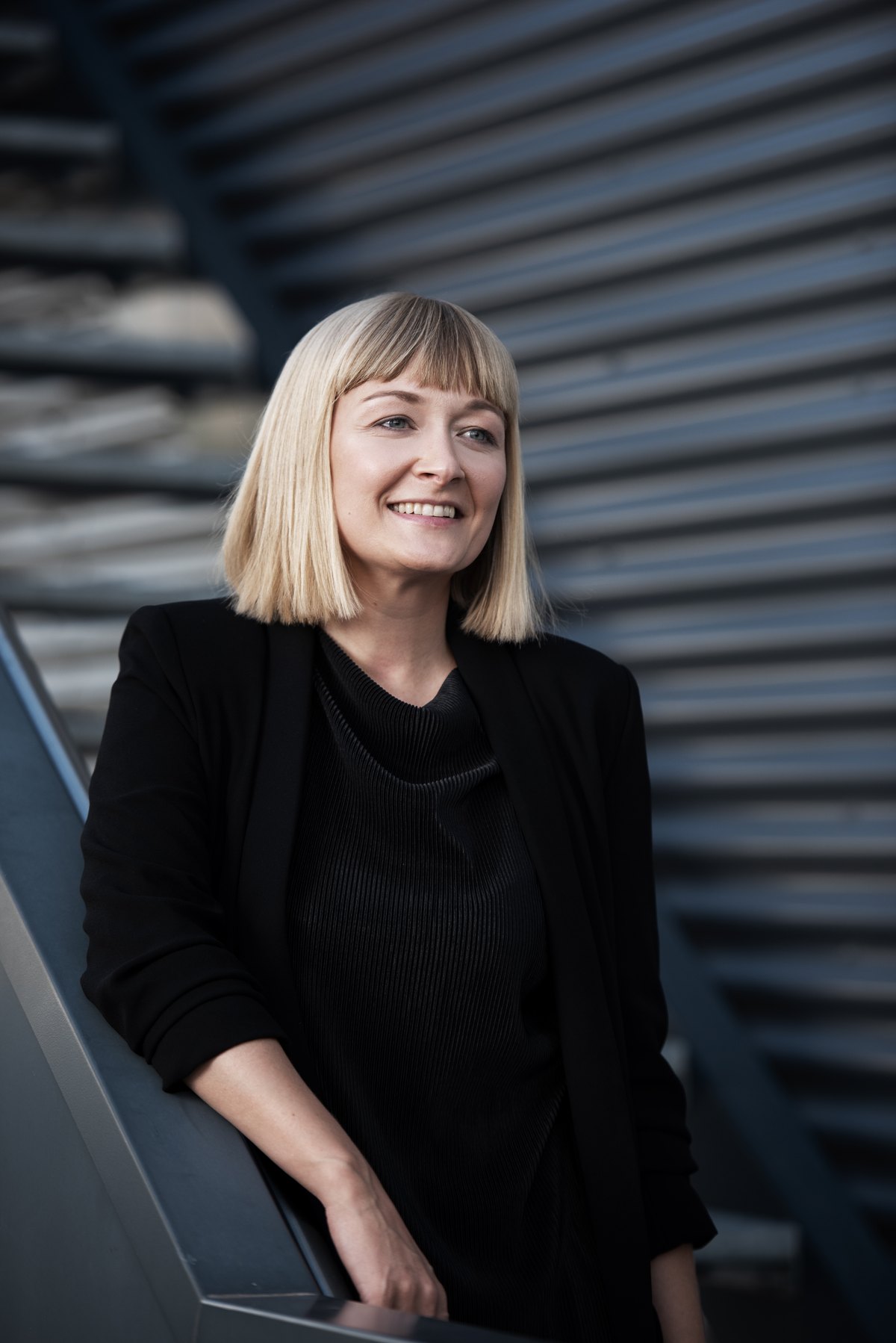 Frau in Schwarz vor silbrig gewellter Metallwand