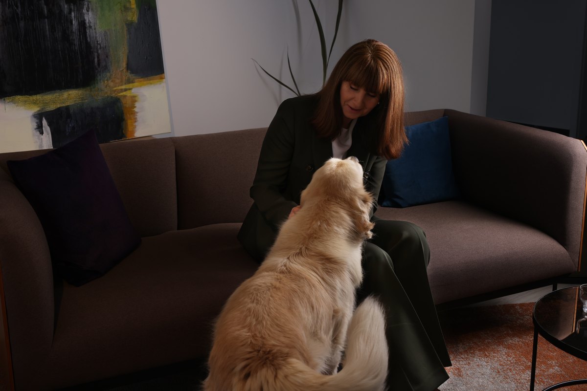 Frau sitzt mit ihrem Hund auf einem Sofa im hellen Wohnraum