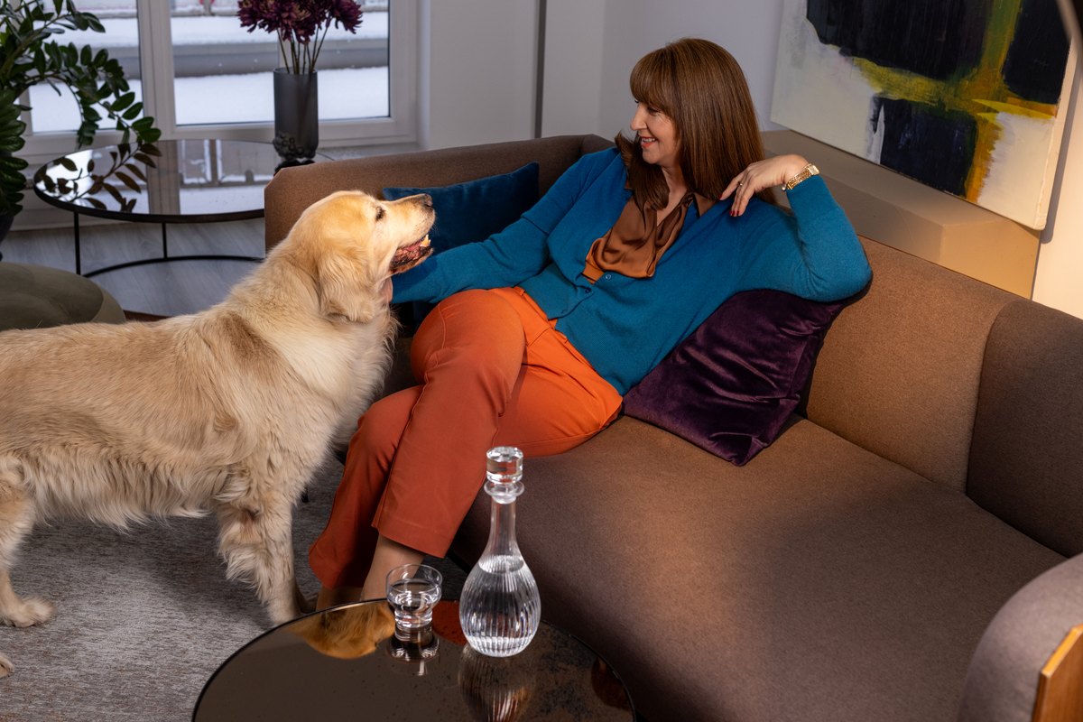 Frau in Blau und Orange liegt mit Hund auf dem Sofa im hellen Raum