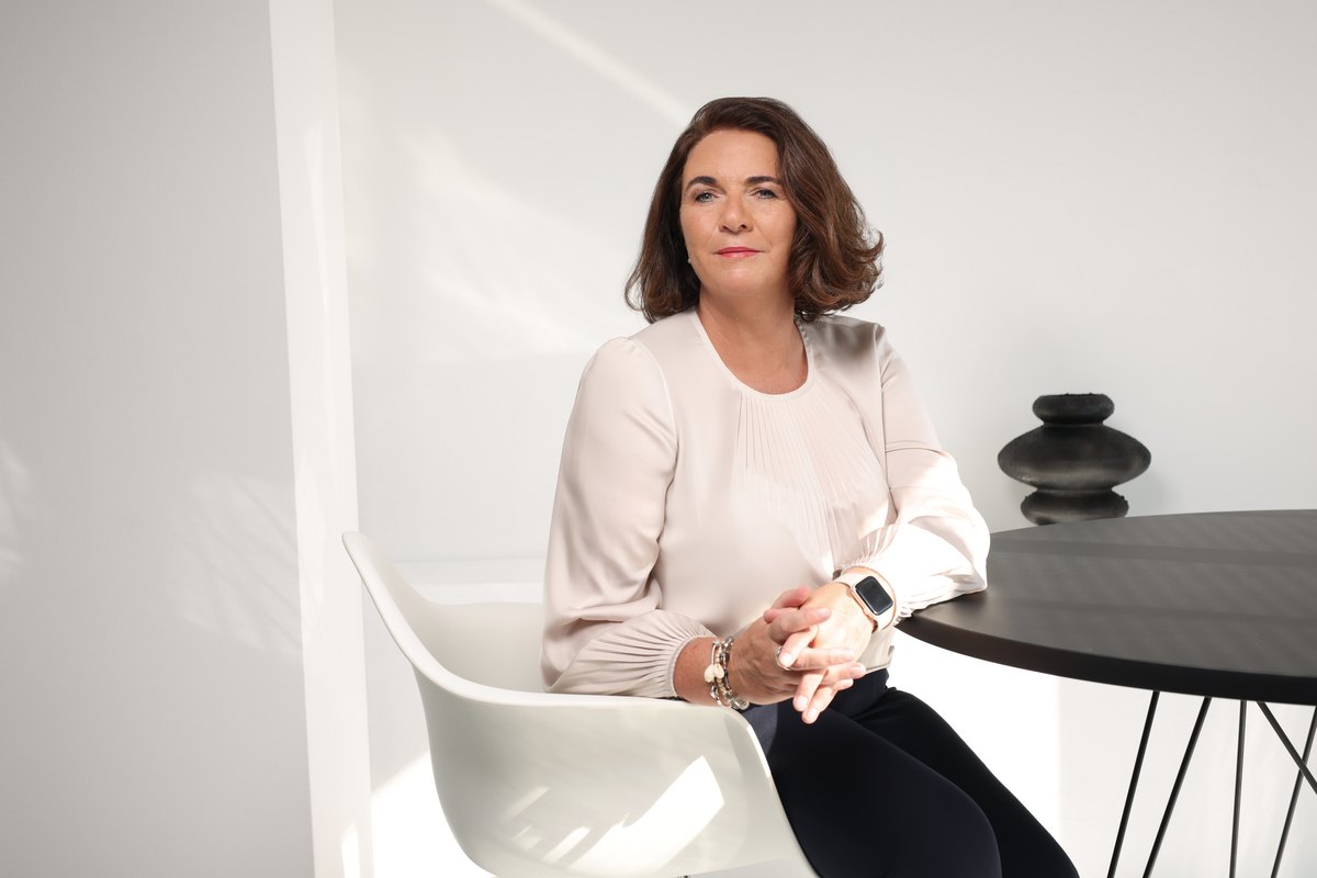 Frau in weißer Bluse sitzt in hellem, minimalistischem Raum