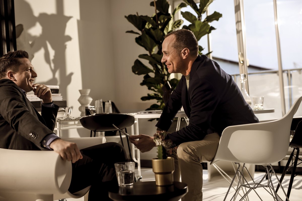 Zwei Männer im Gespräch in heller Lounge mit Pflanzen