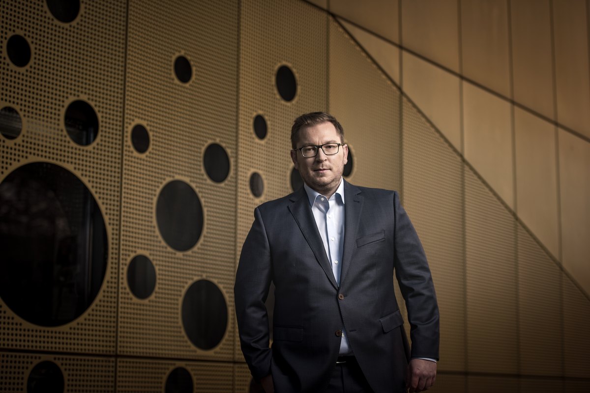 Mann im Anzug vor goldfarbener perforierter Wand