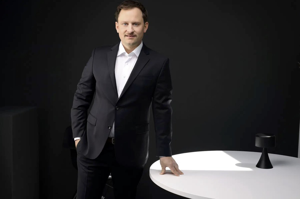 Mann im Anzug steht an einem runden weißen Tisch im dunklen Raum