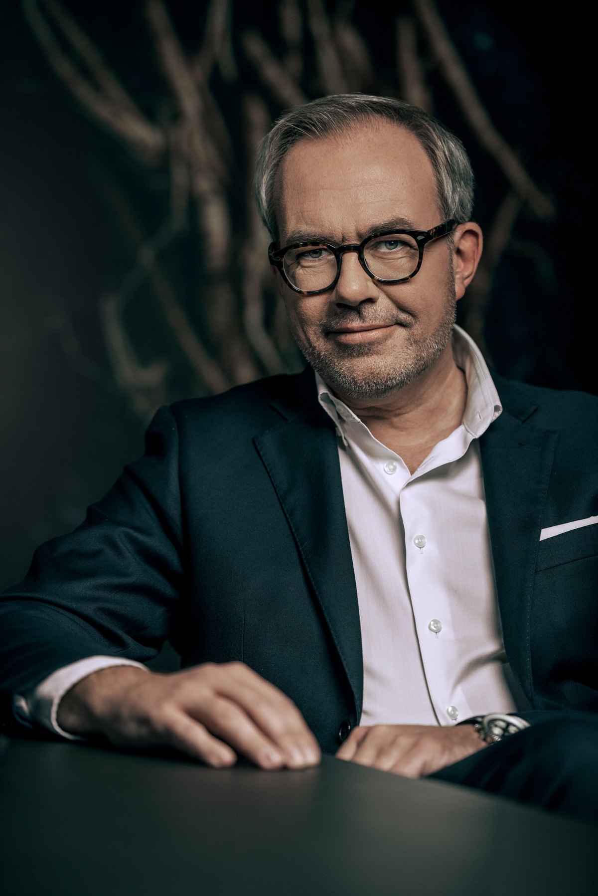 Mann mit Brille im grünen Sakko stützt sich auf einen Tisch