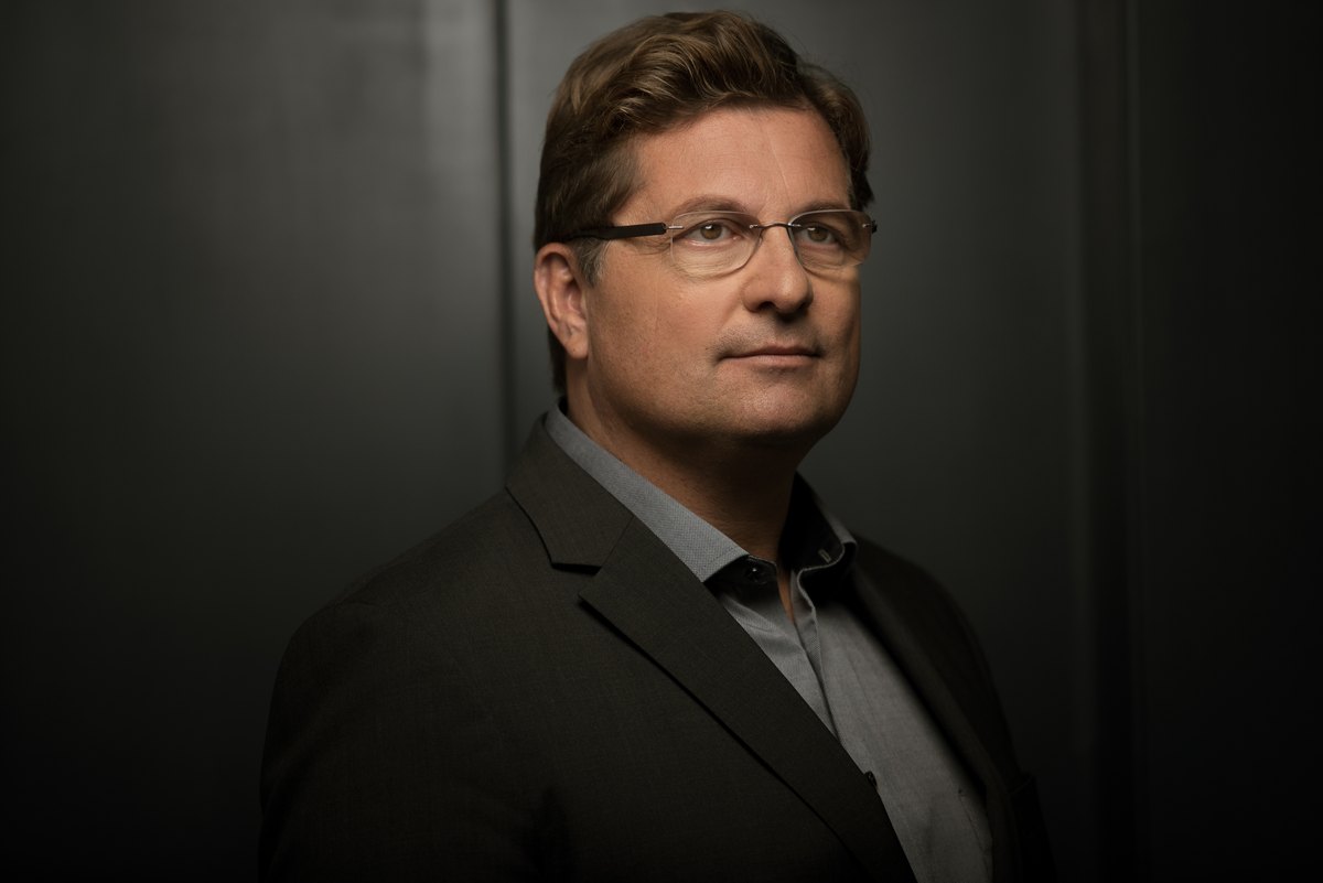 Mann mit Brille im grauen Sakko vor dunklem Hintergrund