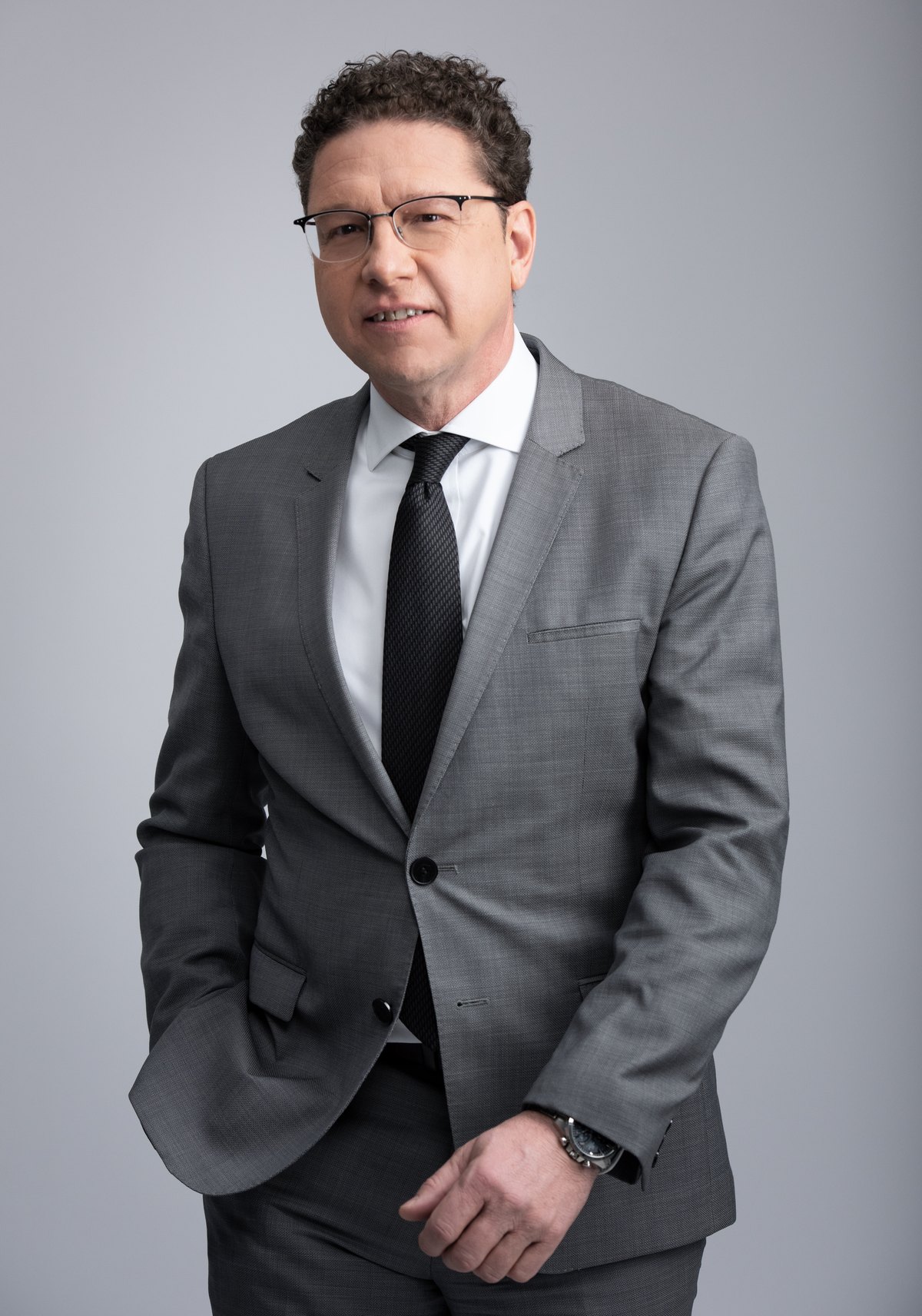 Mann im grauen Anzug mit Brille vor hellem Hintergrund