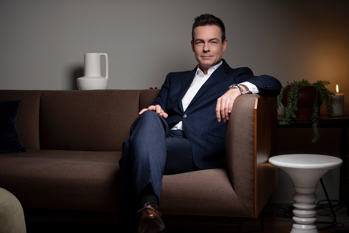 Mann im dunklen Anzug sitzt auf einem Sofa in dunkler Lounge
