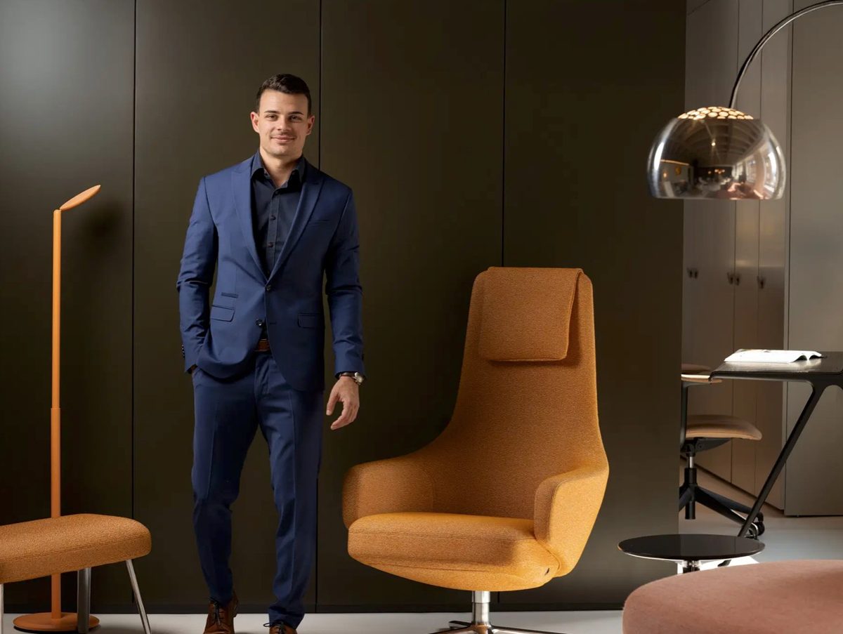 Businessportrait eines Mannes im blauen Anzug zwischen orangefarbenen Designsesseln