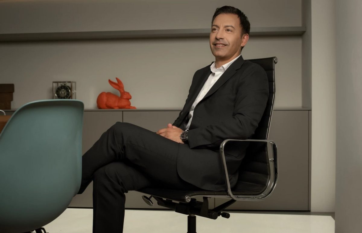 Businessportrait eines sitzenden Mannes im dunklen Anzug auf einem Drehstuhl in einem modernen Büro