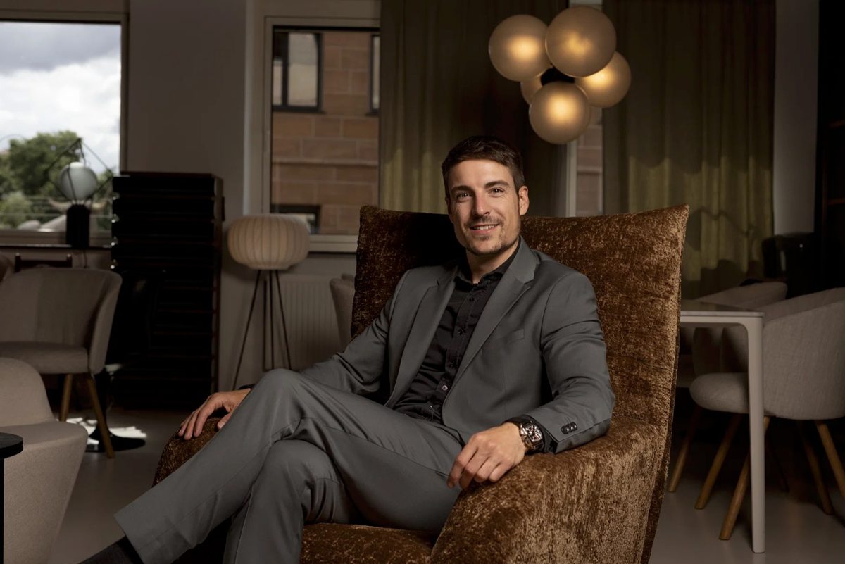 Businessportrait eines Mannes im grauen Anzug, sitzend in einem braunen Samtsessel in einer Lounge