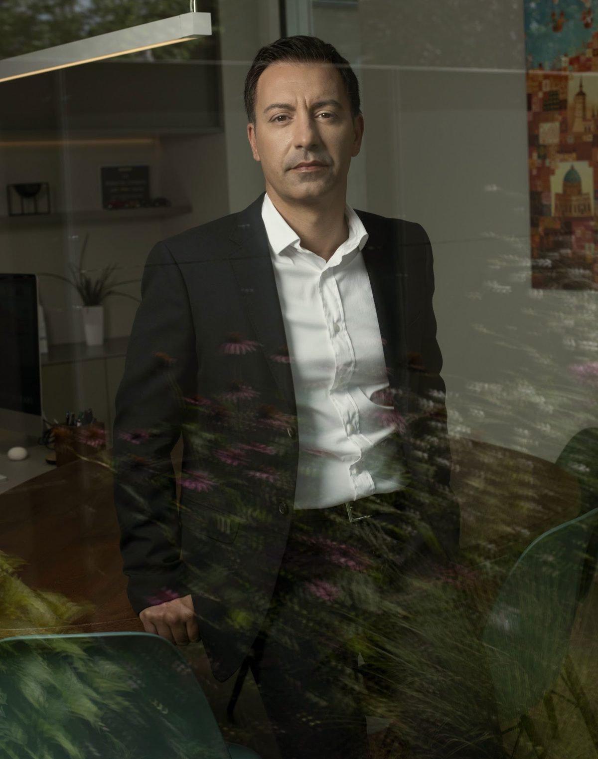 Businessportrait eines Mannes im schwarzen Anzug durch eine Glasscheibe mit Pflanzenspiegelung fotografiert