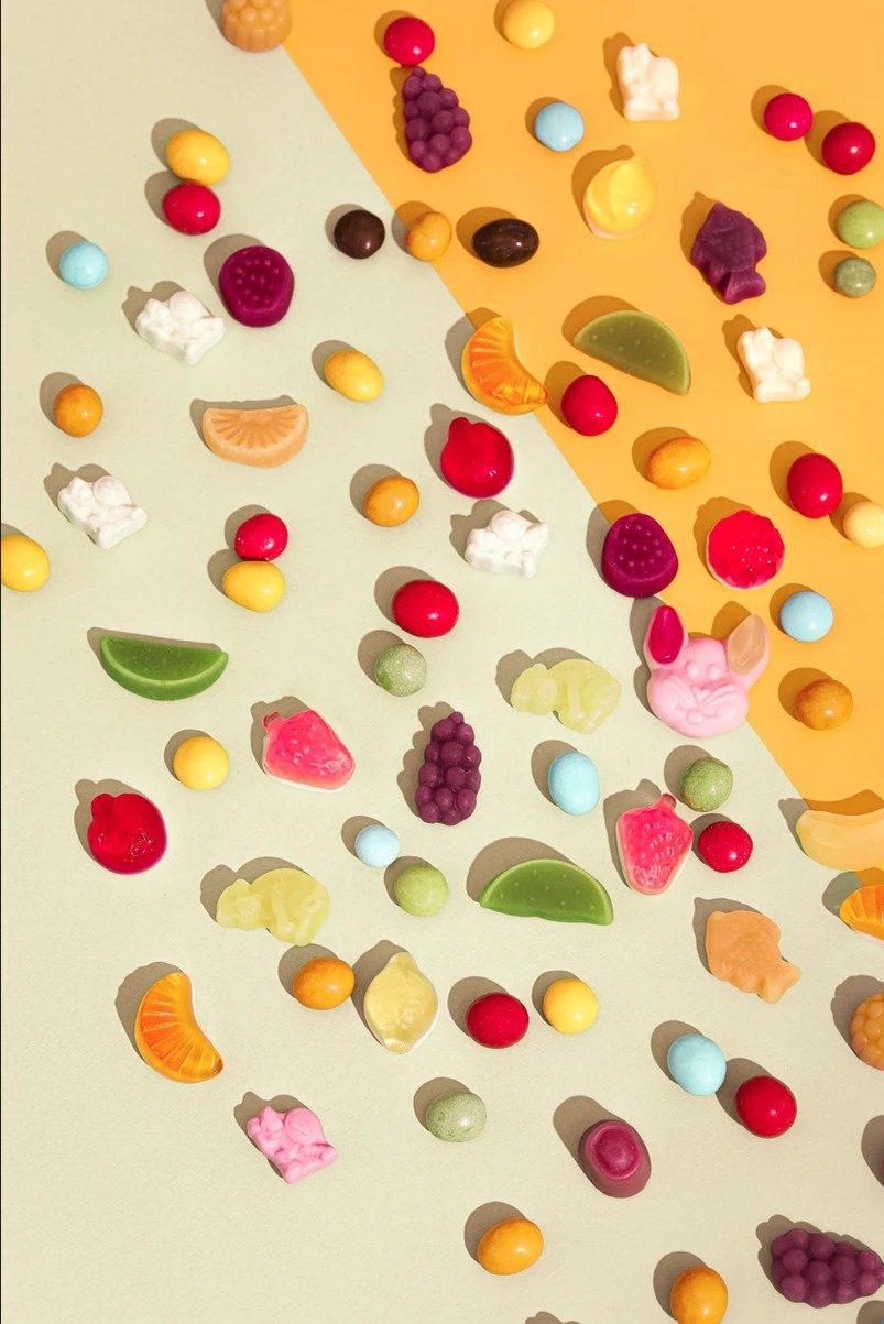Bunte Frucht- und Geleebonbons im Raster auf grün-orangem Hintergrund von oben fotografiert