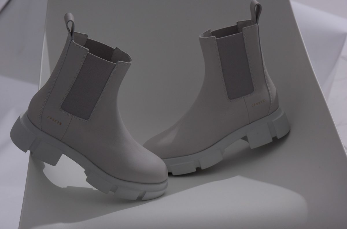 Zwei helle Chelsea Boots auf gefaltetem weißem Papier im weichen Studiolicht
