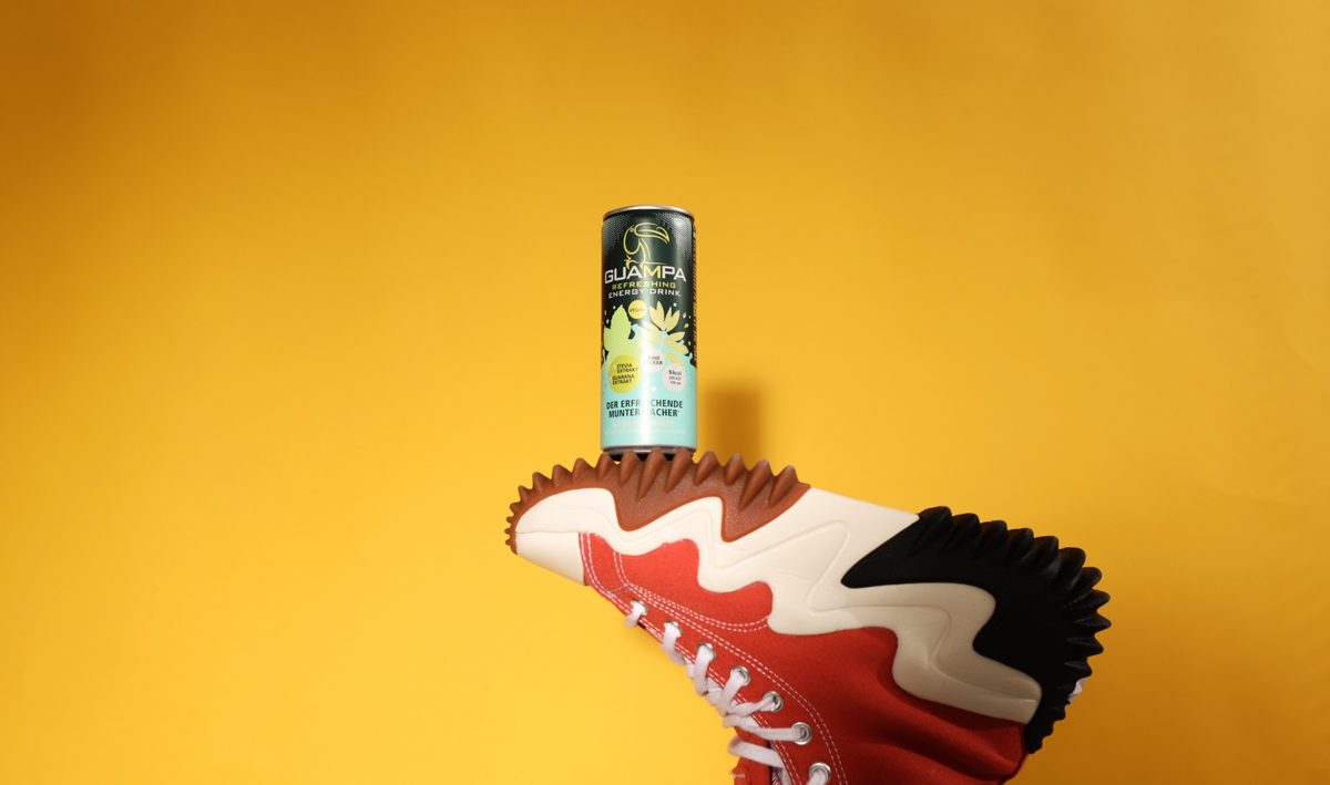 Getränkedose balanciert auf einer Sneakersohle vor gelbem Hintergrund