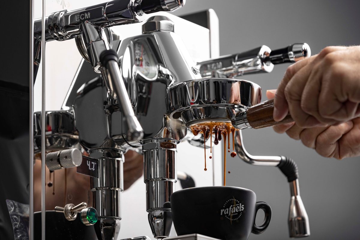 Nahaufnahme einer verchromten Espressomaschine, aus der Kaffee in eine schwarze Tasse läuft