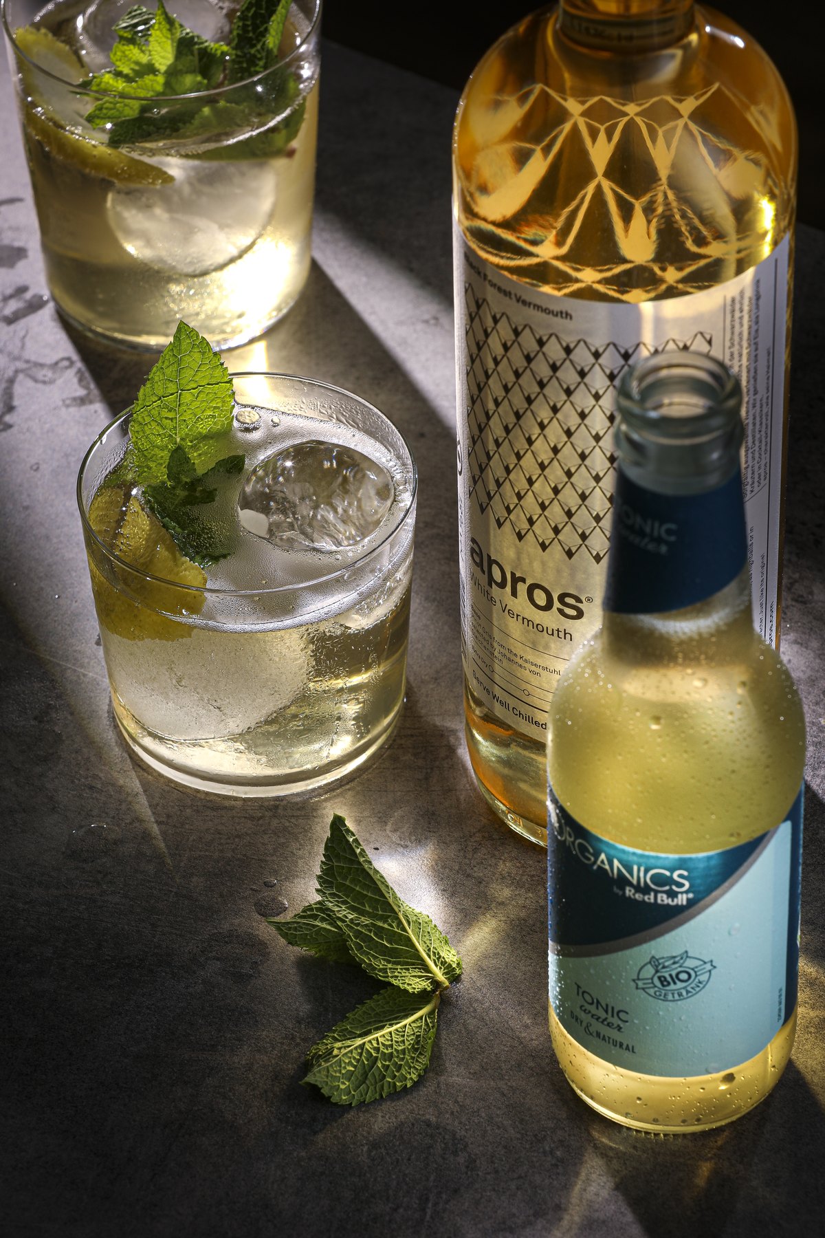 Gin-Flasche mit zwei Gläsern, Minze und Limette im Streiflicht