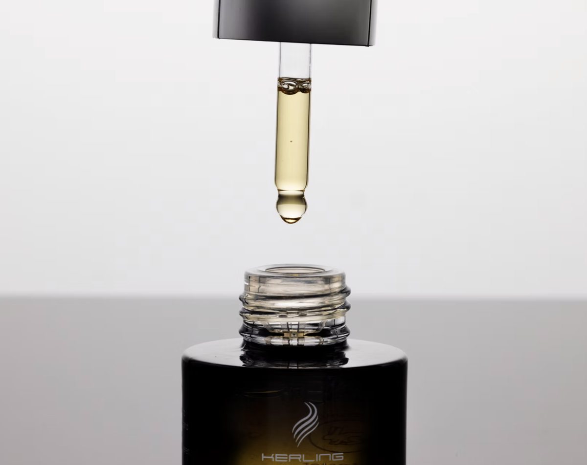 Pipette mit goldenem Haaröl über geöffneter Flasche, Studioaufnahme