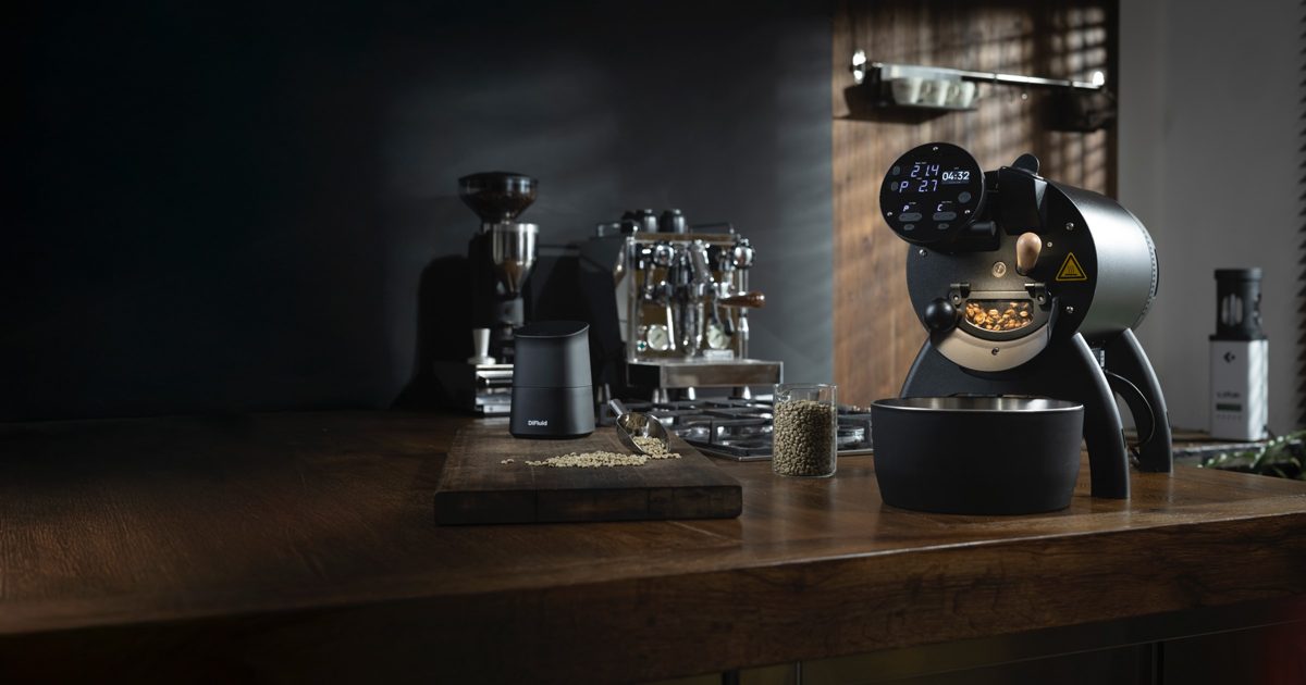 Schwarzer Kaffeeröster mit leuchtendem Display auf einer Holztheke vor dunklem Hintergrund
